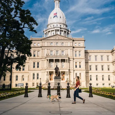 Woman walking a dog in front of the State of Michigan capitol building
